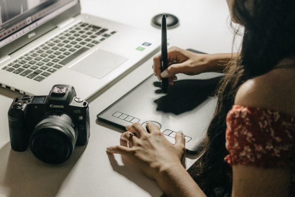 Close-up of a woman using a graphics tablet to create digital art with a laptop.